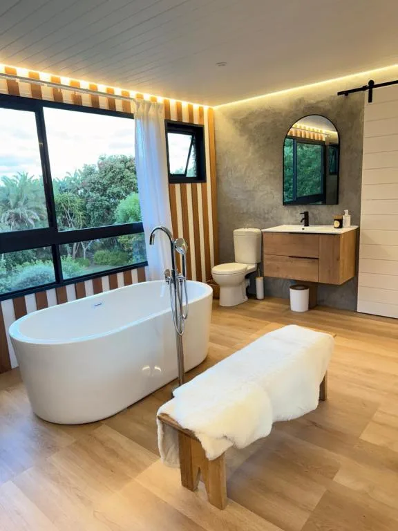 Modern bathroom with freestanding white tub and wooden vanity overlooking garden