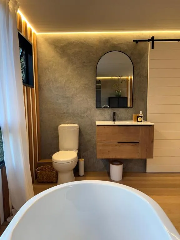 Modern bathroom with freestanding tub, wooden vanity, arched mirror, and ambient lighting