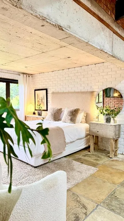 Bright brick bedroom with white bedding, plants, and natural light from windows