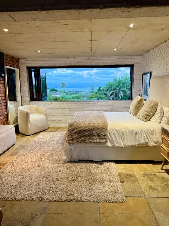 Spacious bedroom with king bed, armchair, and large window overlooking coastal landscape
