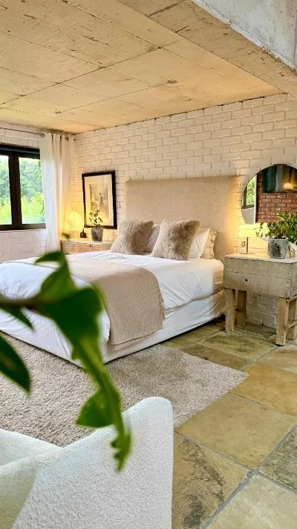 Bright bedroom with double bed, white linens, brick walls, and potted plant