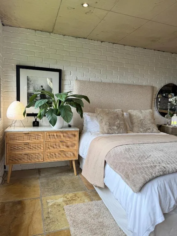 Modern bedroom with upholstered headboard, wooden nightstand, and potted plants
