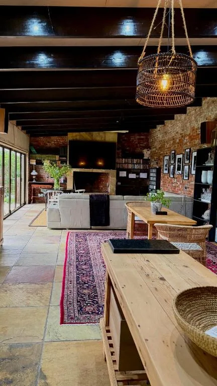 Open-plan lounge with exposed brick, fireplace, wooden dining tables, and woven pendant lighting