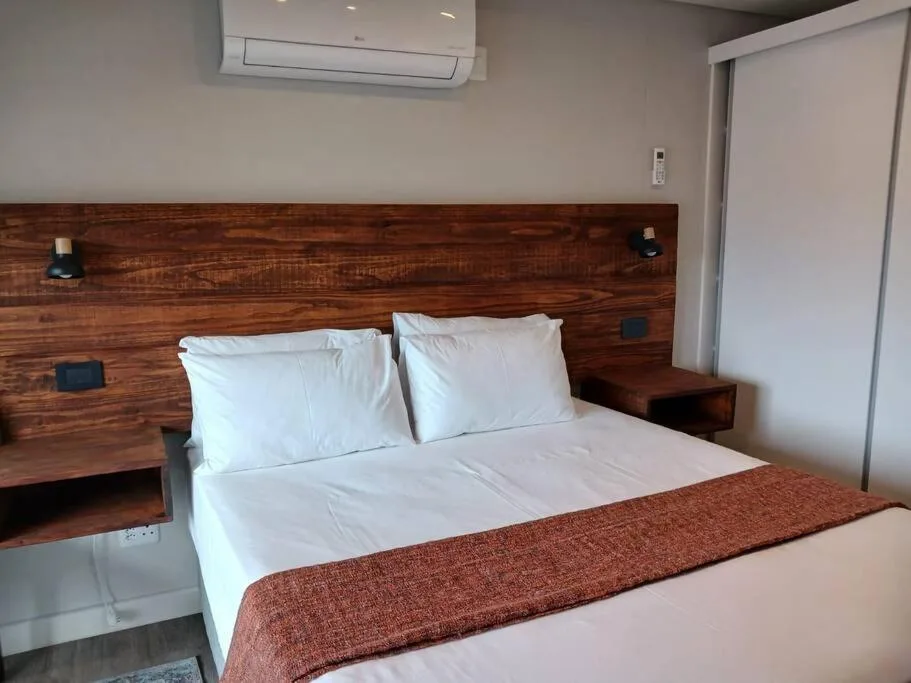 Modern bedroom with wooden headboard, white linens, and air conditioning unit