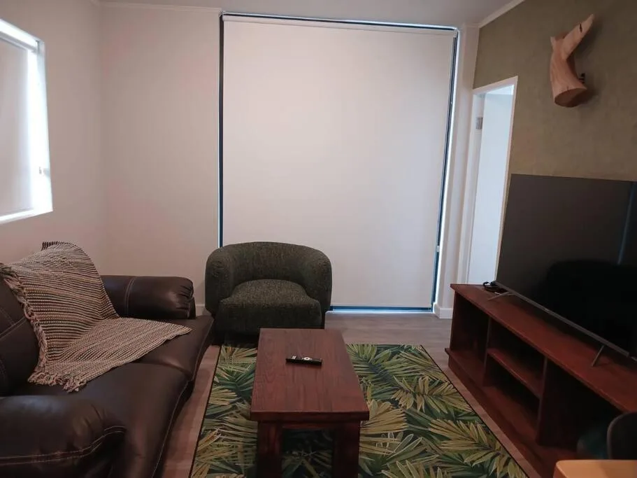 Living room with leather sofa, armchair, wooden coffee table, and wall-mounted TV