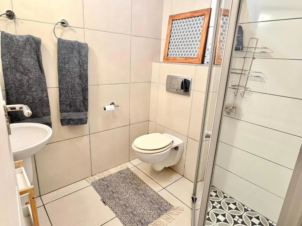 Clean bathroom with white tiles, toilet, sink, shower enclosure and dark towels