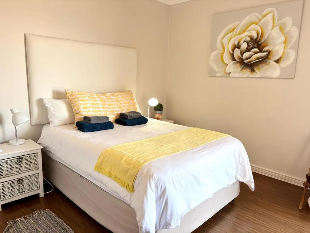 Bright bedroom with white linens, yellow accents, and floral wall art