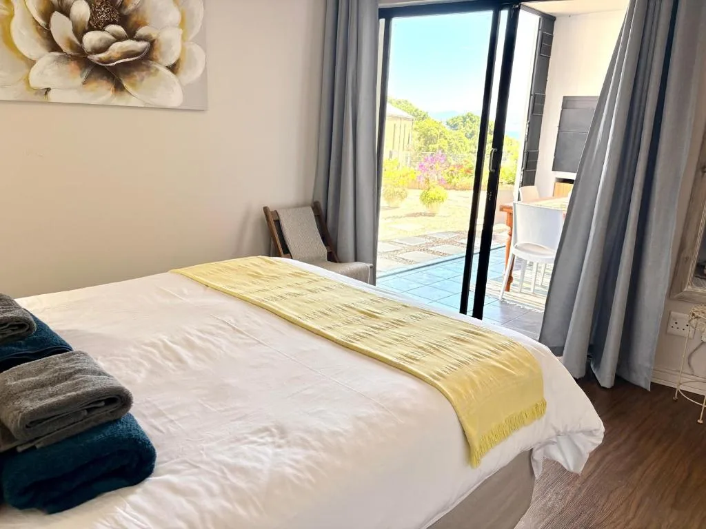 Bright bedroom with queen bed, garden views through glass doors, and yellow throw