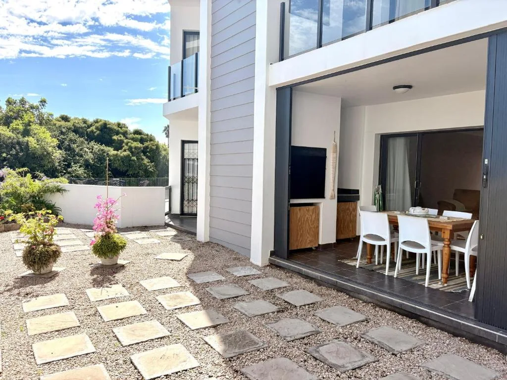 Modern patio with paving stones, flowering plants, and dining setup overlooking garden