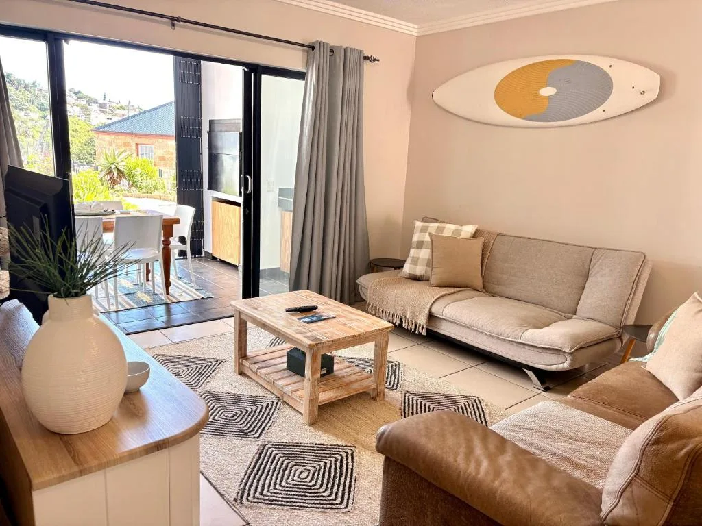 Spacious lounge with beige sofa, leather armchair, wooden coffee table, and sea view doors