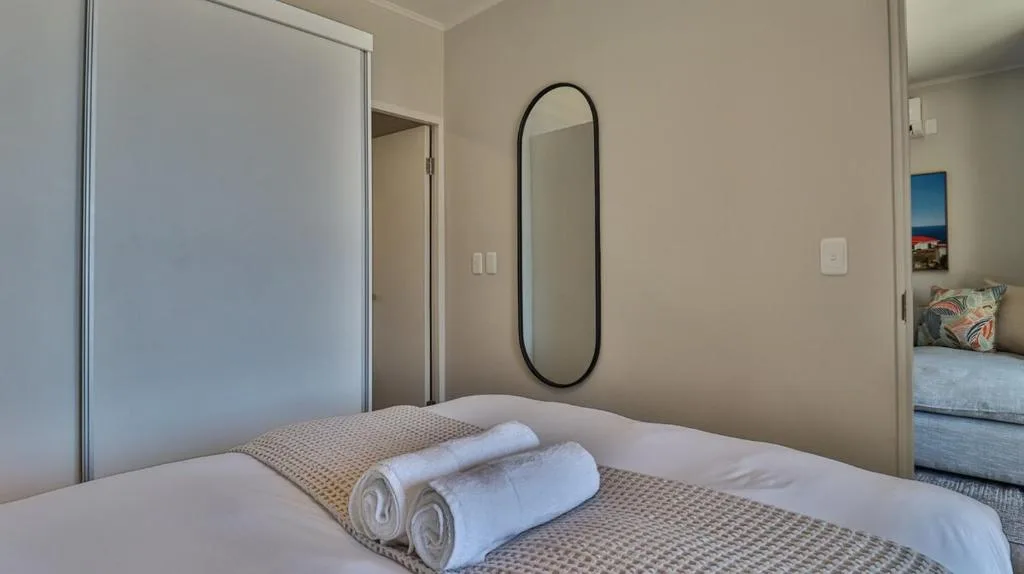 Modern bedroom with neatly rolled towels on bed and elegant oval mirror