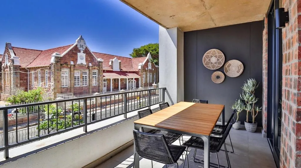 Covered outdoor balcony with dining table overlooking historic building and gardens