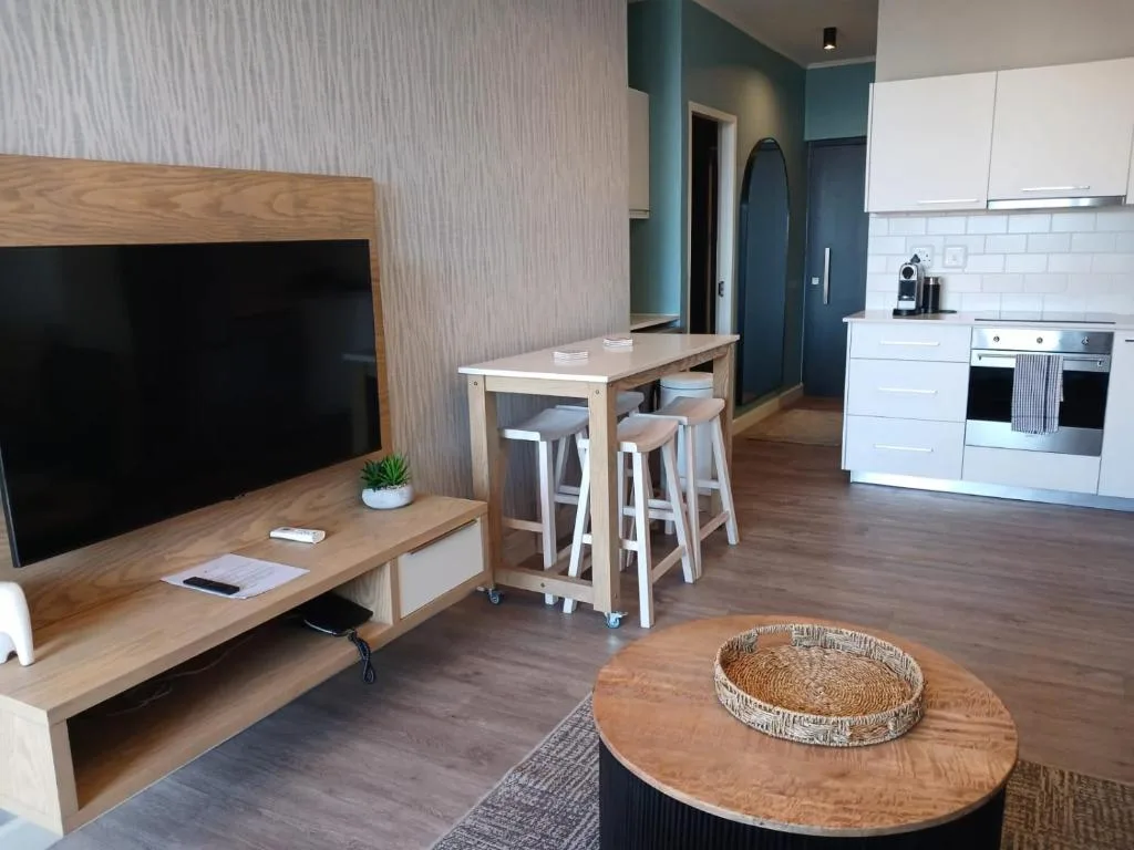 Modern open-plan lounge with TV, dining counter, and kitchen visible