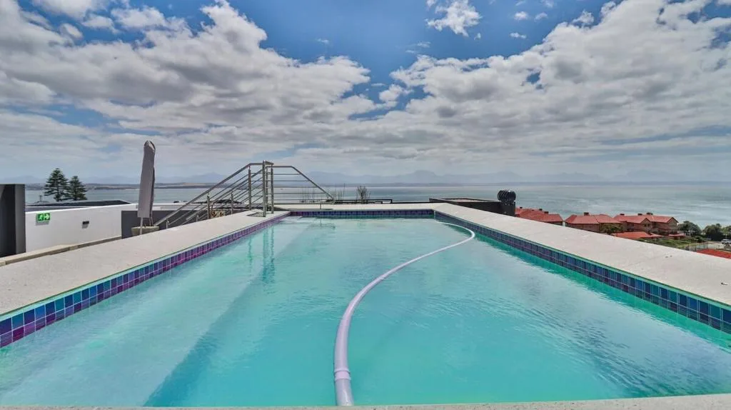 Sparkling turquoise swimming pool with ocean and mountain views beyond