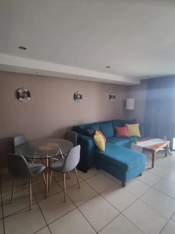 Open-plan lounge with blue sofa, colorful cushions, and small dining table