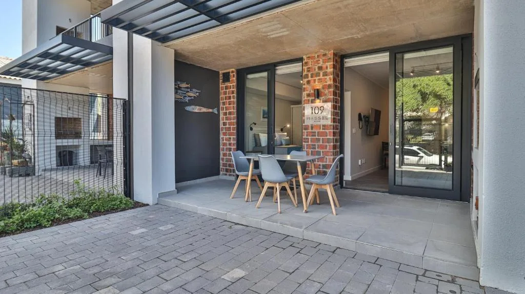 Covered patio with dining table and blue chairs overlooking garden