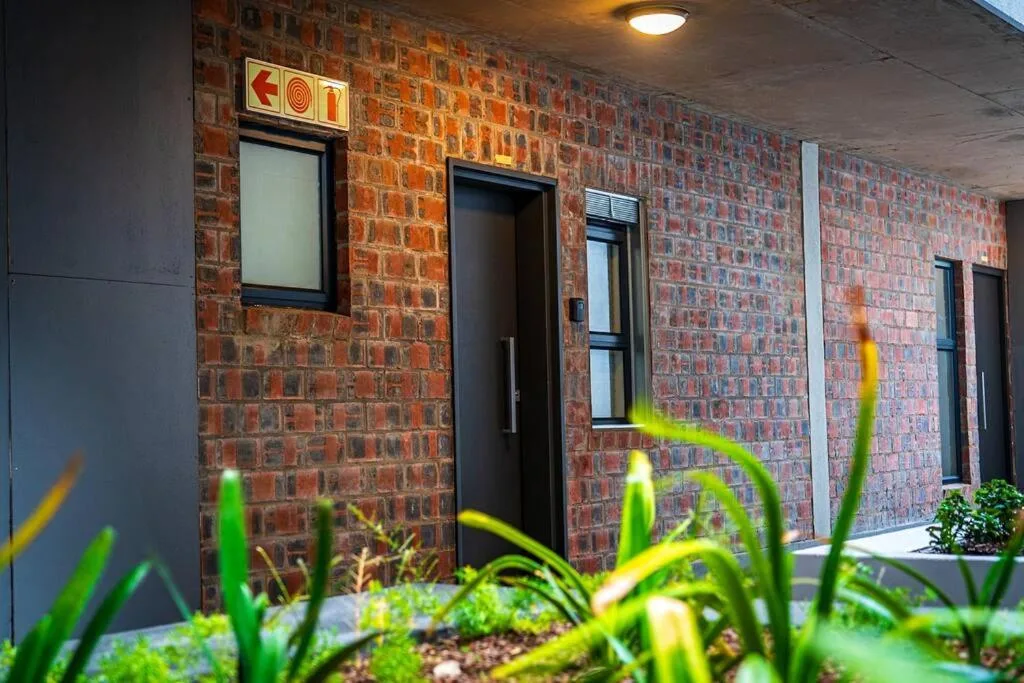 Modern brick building facade with black doors and planted garden bed