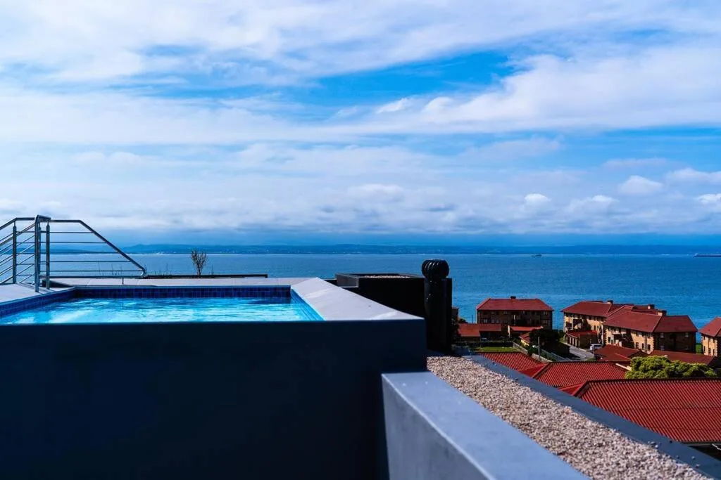 Modern infinity pool overlooking ocean and coastal village below