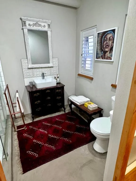 Stylish bathroom with vanity, mirror, toilet, and burgundy rug