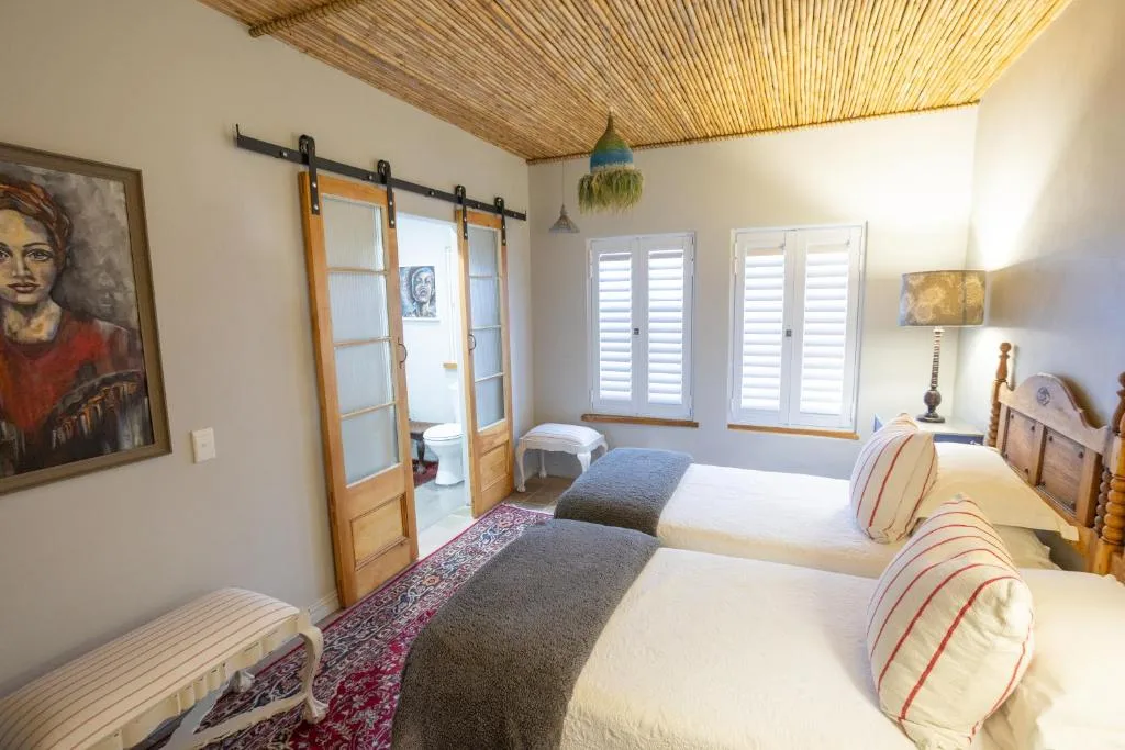 Bright bedroom with two twin beds, wooden barn doors, and white shutters