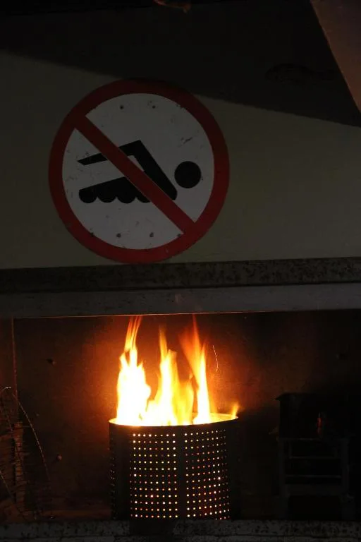No-swimming sign above lit outdoor fire basket at night