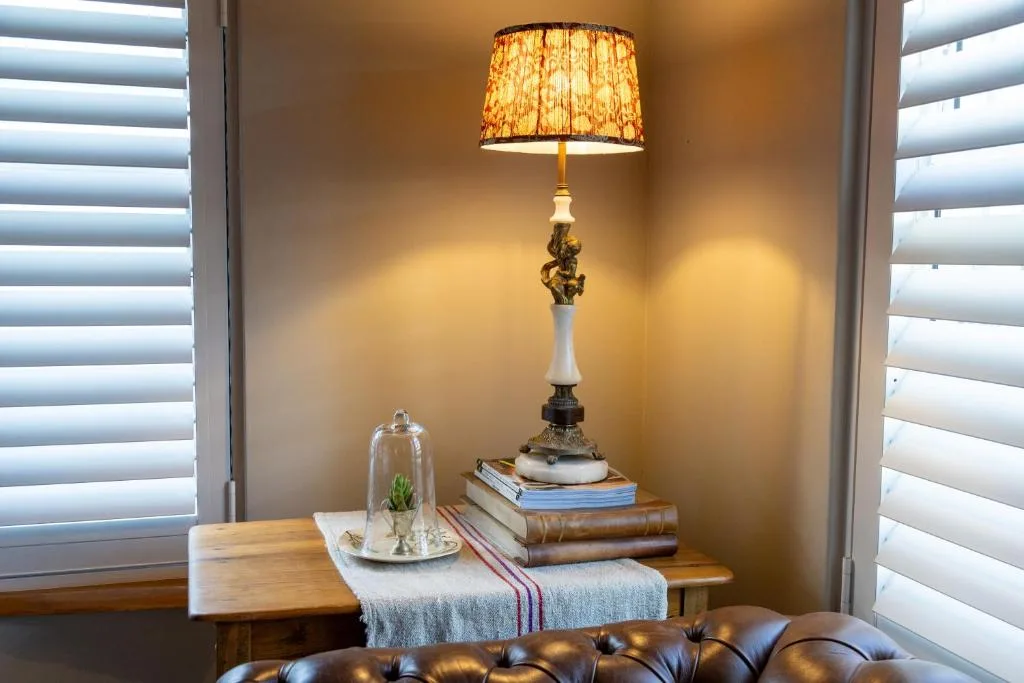 Elegant decorative lamp and books on wooden table with shuttered windows