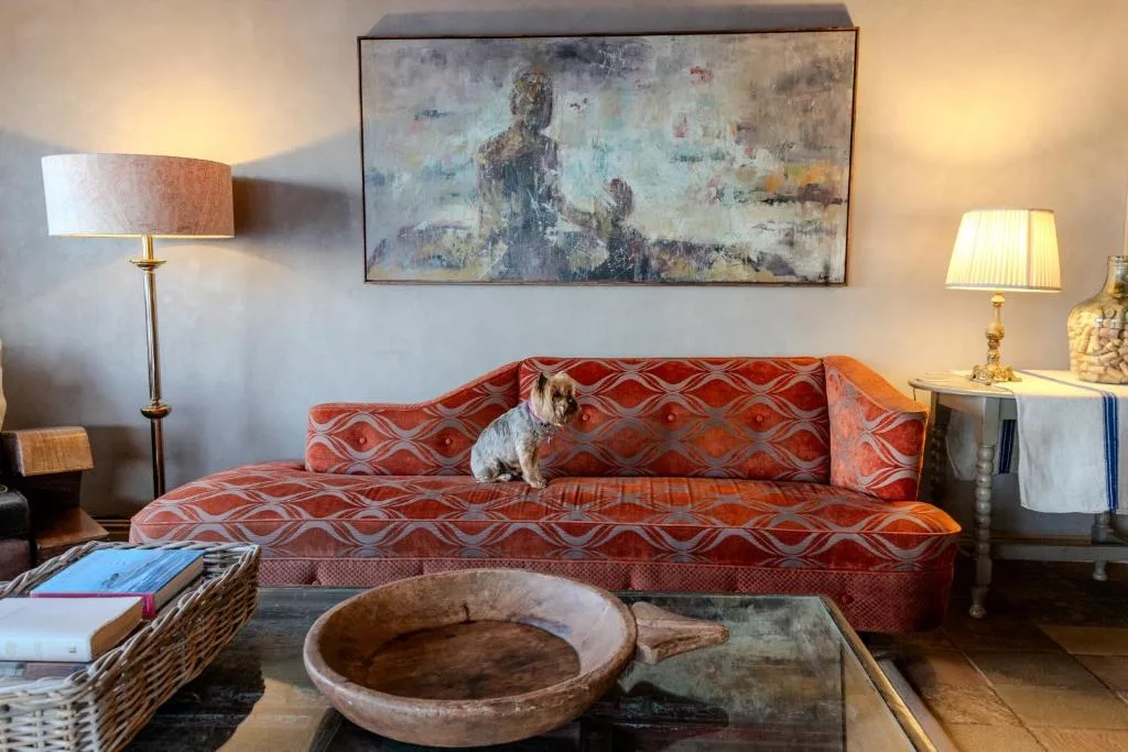 Living room with red patterned sofa, artwork, lamps, and rustic decor