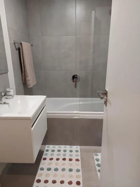 Modern bathroom with glass-enclosed shower, white vanity sink, and tiled walls