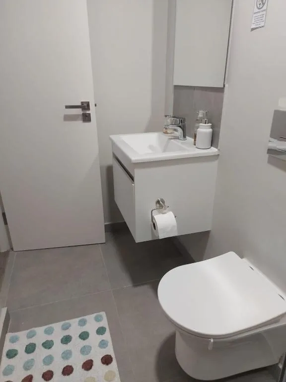 Modern bathroom with white vanity sink, toilet, and grey tiled flooring