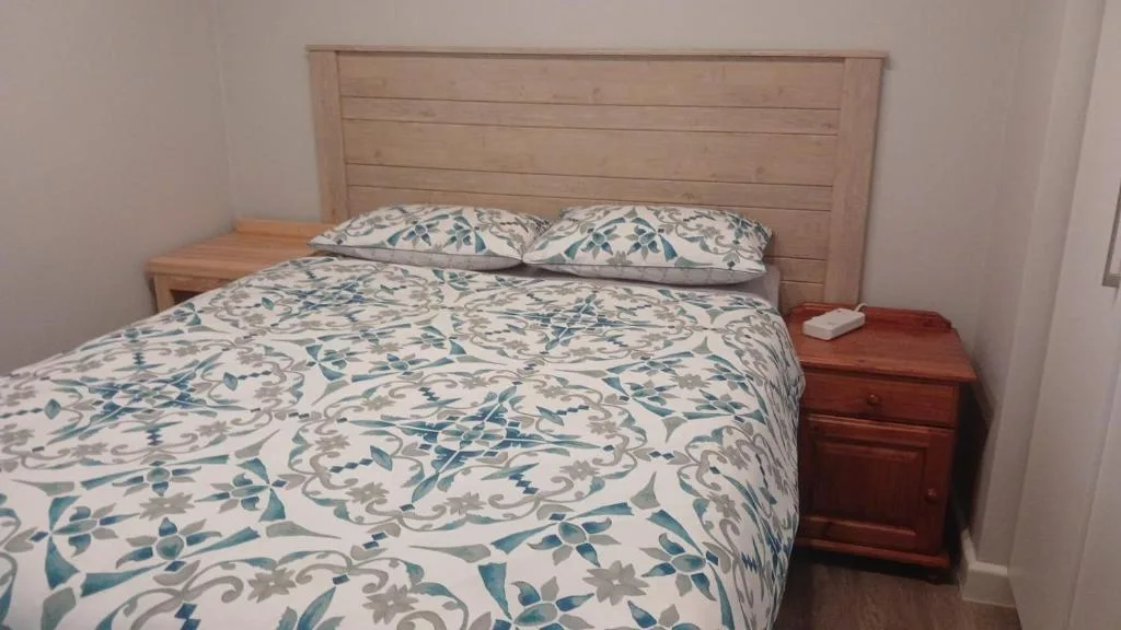 Double bed with patterned bedding and wooden headboard in bright room