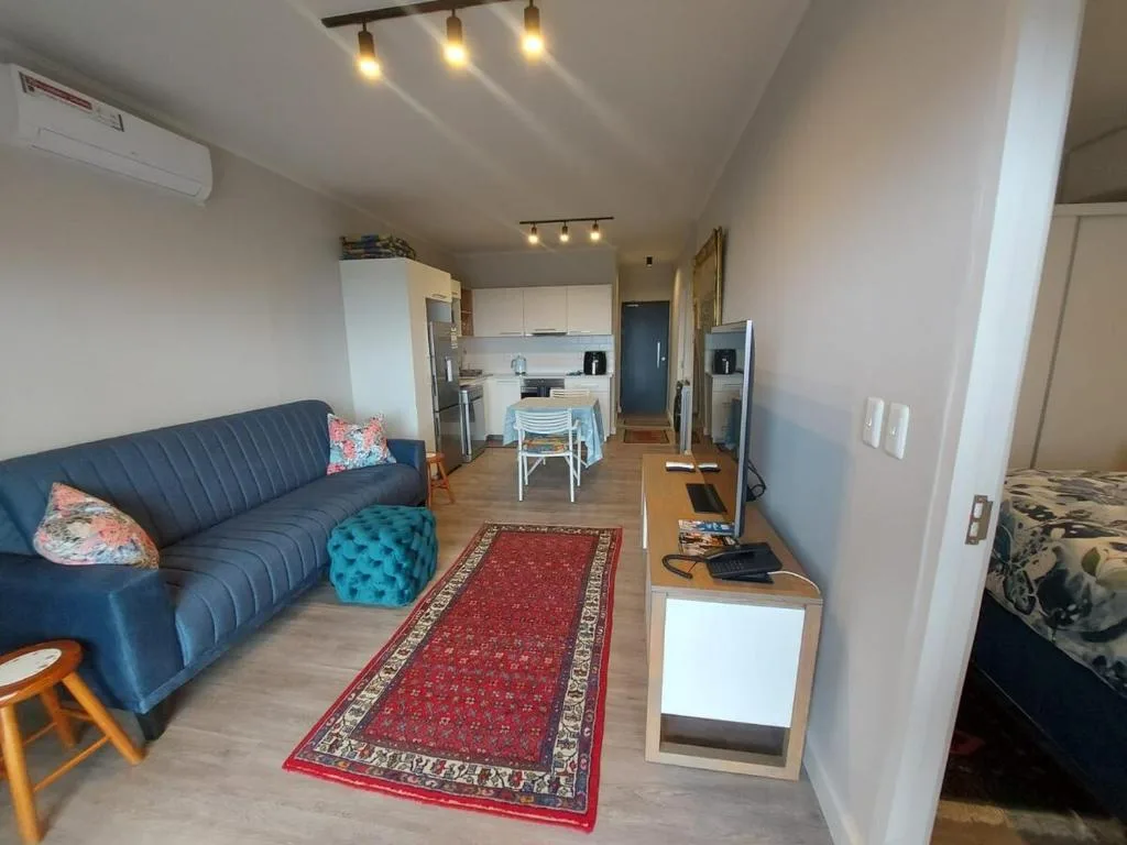 Open-plan lounge with navy sofa, kitchen visible beyond, bedroom on right
