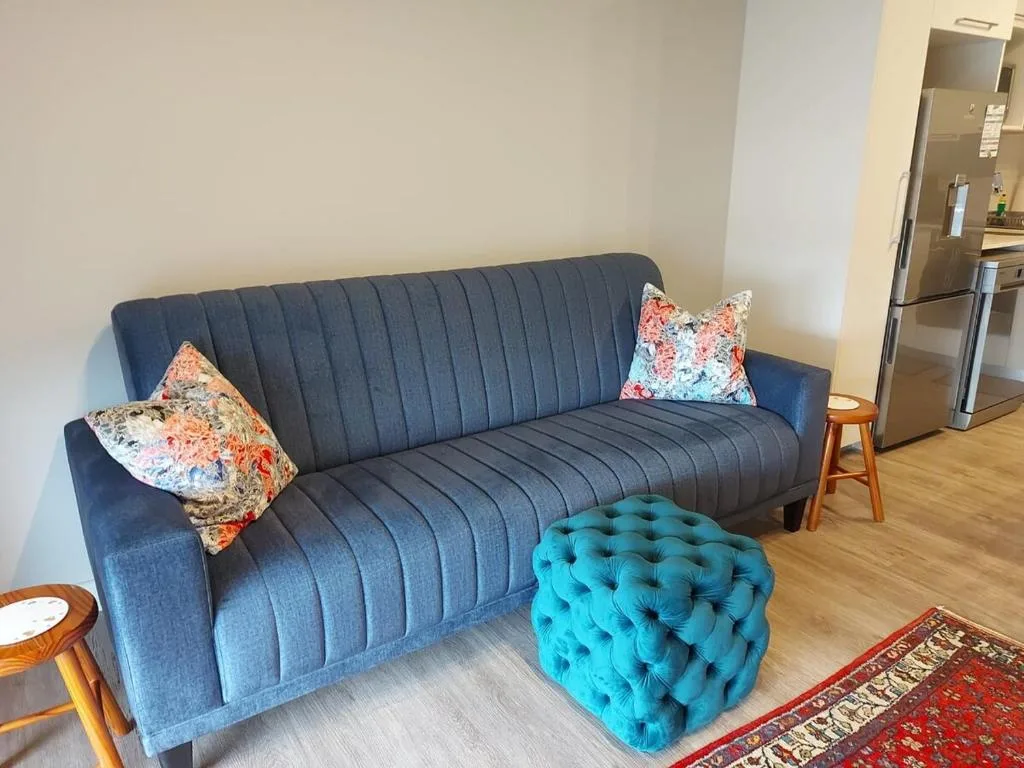 Modern blue sofa with colorful pillows and turquoise ottoman in living area