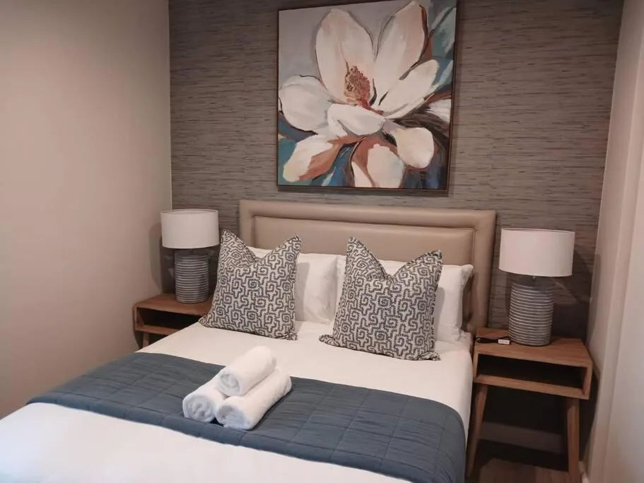 Modern bedroom with upholstered headboard, patterned pillows, and floral wall art