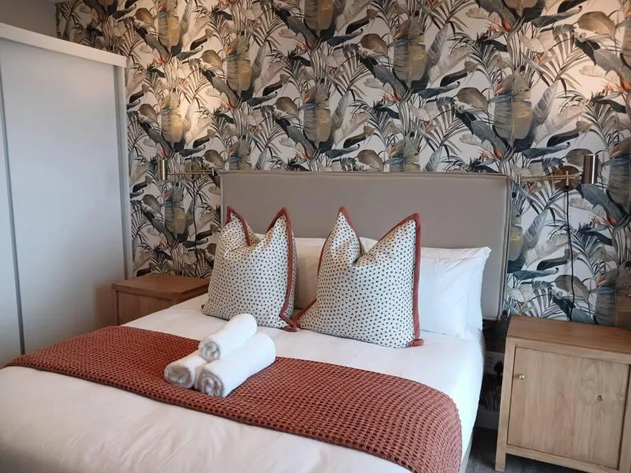 Stylish bedroom with patterned wallpaper, decorative pillows, rolled towels on bed