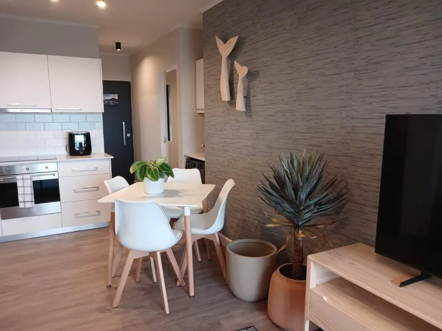 Modern dining table with white chairs and kitchen visible in background