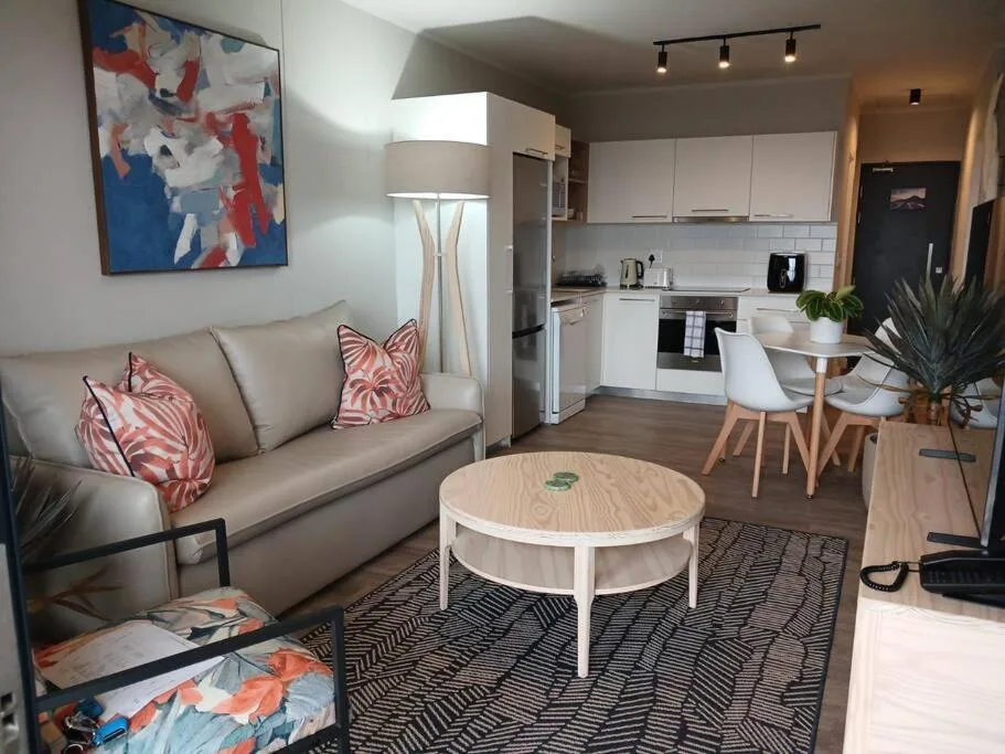 Modern lounge with beige sofa, patterned cushions, and open-plan kitchen view