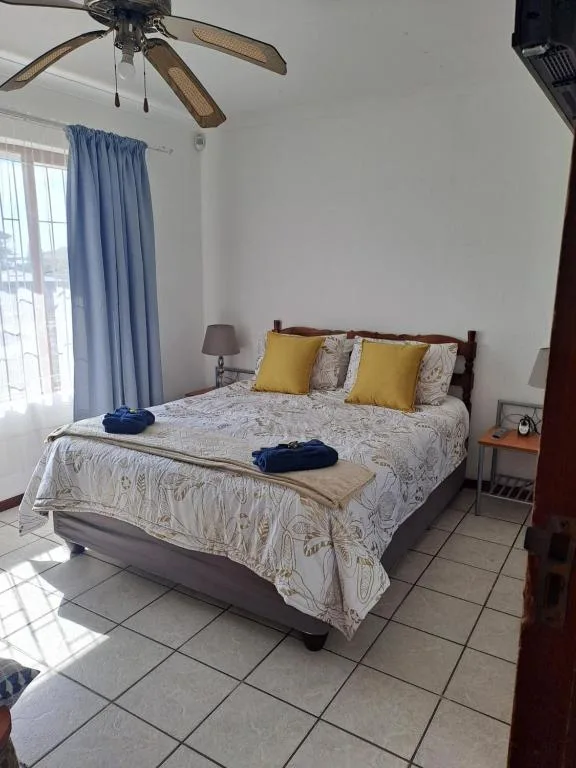 Bright bedroom with double bed, yellow cushions, ceiling fan, blue curtains