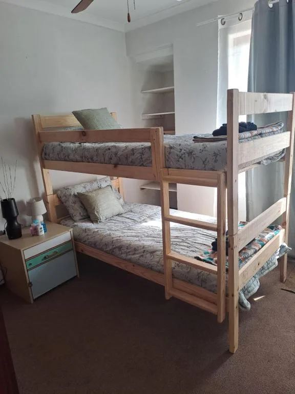 Bright bedroom with wooden bunk beds and patterned mattresses, bedside table