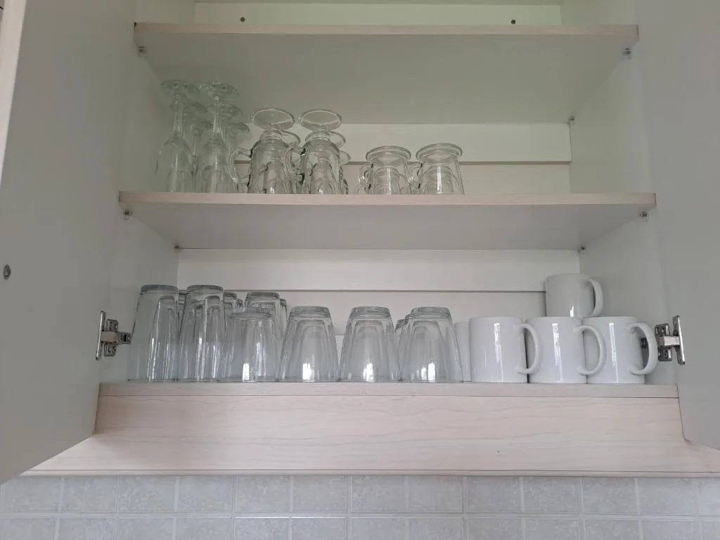 Open kitchen cabinet displaying glass jars and white ceramic mugs neatly organized