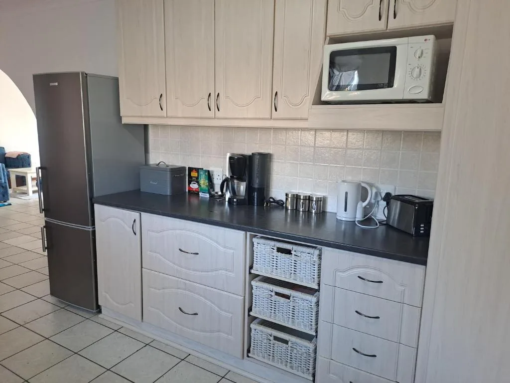 Modern kitchen with white cabinetry, black countertop, stainless steel fridge, microwave, and appliances