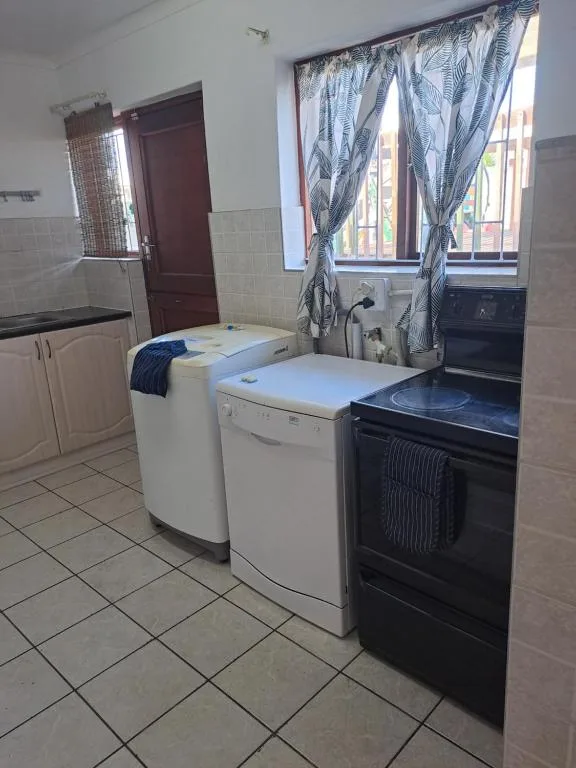 Kitchen with washer, dryer, stove, and window with patterned curtains