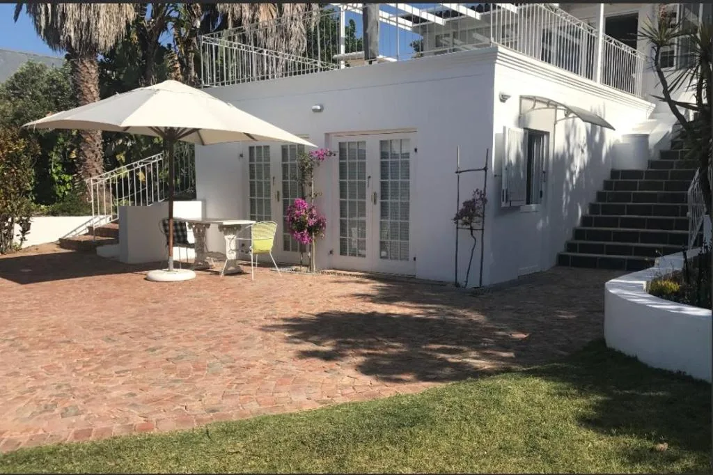 White apartment building with brick patio, umbrella, and flowering plants