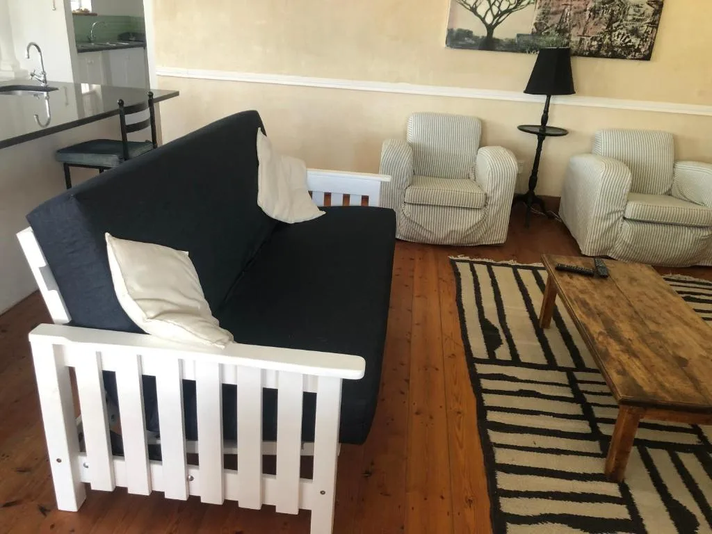 Comfortable lounge with black sofa, cream armchairs, wooden floors, striped rug