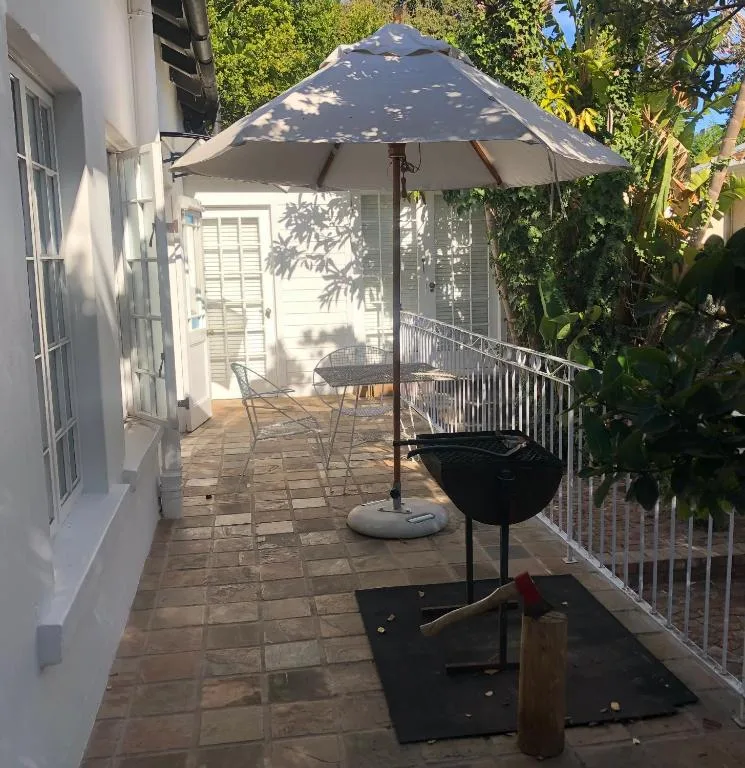 Shaded patio with umbrella, seating, and braai area surrounded by greenery