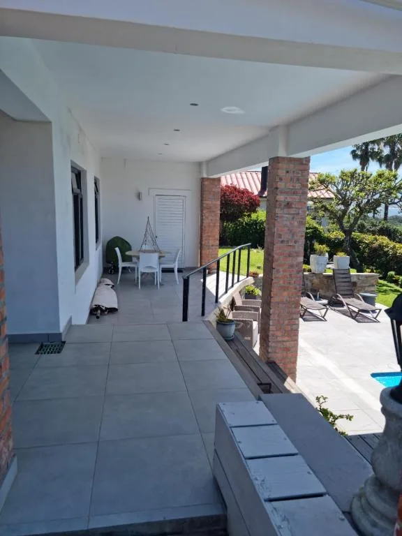 Covered patio with seating area overlooking gardens and pool