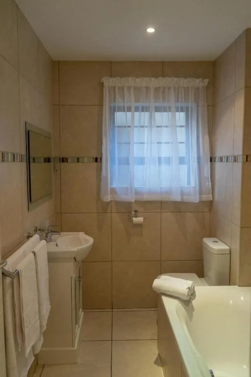 Modern bathroom with bathtub, pedestal sink, toilet, and window with sheer curtains