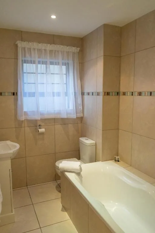 Spacious bathroom with bathtub, toilet, and window with sheer curtains