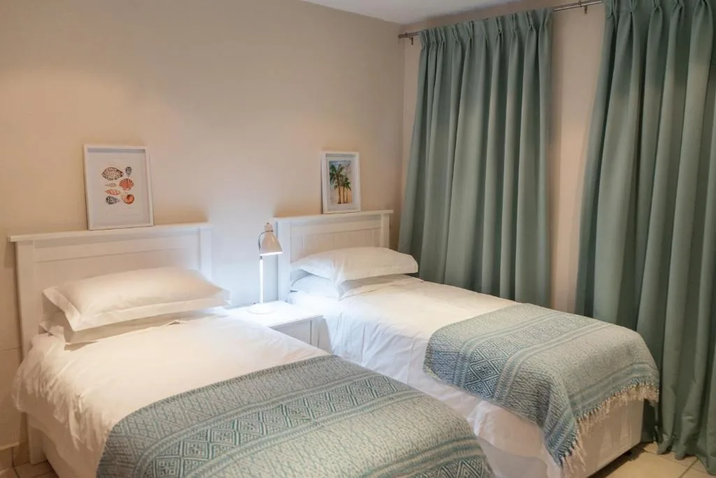 Twin bedroom with white headboards, green curtains, and neutral bedding