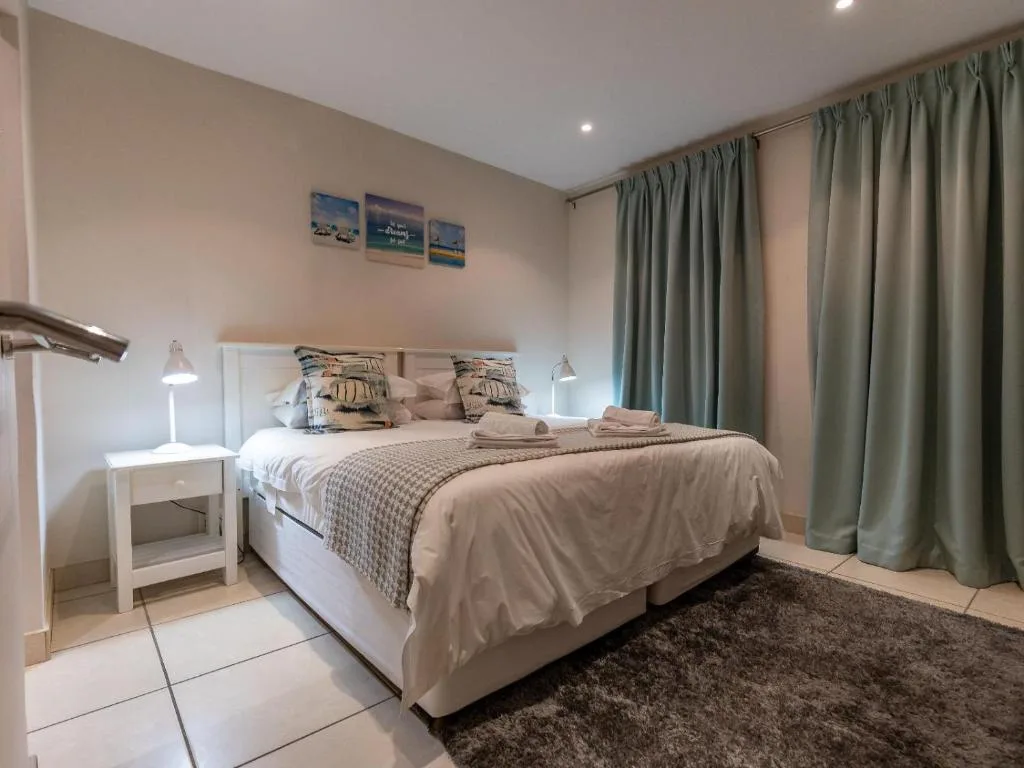 Spacious bedroom with queen bed, white bedside table, and sage green curtains