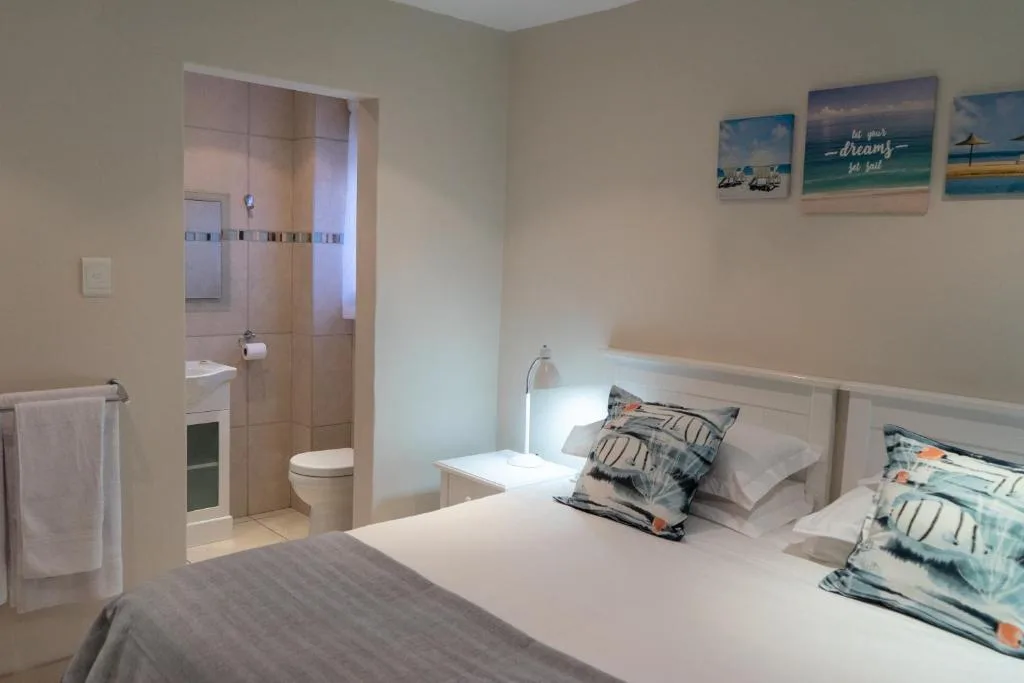 Bright bedroom with queen bed, en-suite bathroom, and coastal wall art
